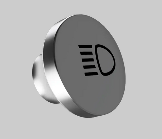 A round metallic car headlight switch knob with a black icon of a light beam and a D-shaped symbol on its face, shown against a solid gray background.